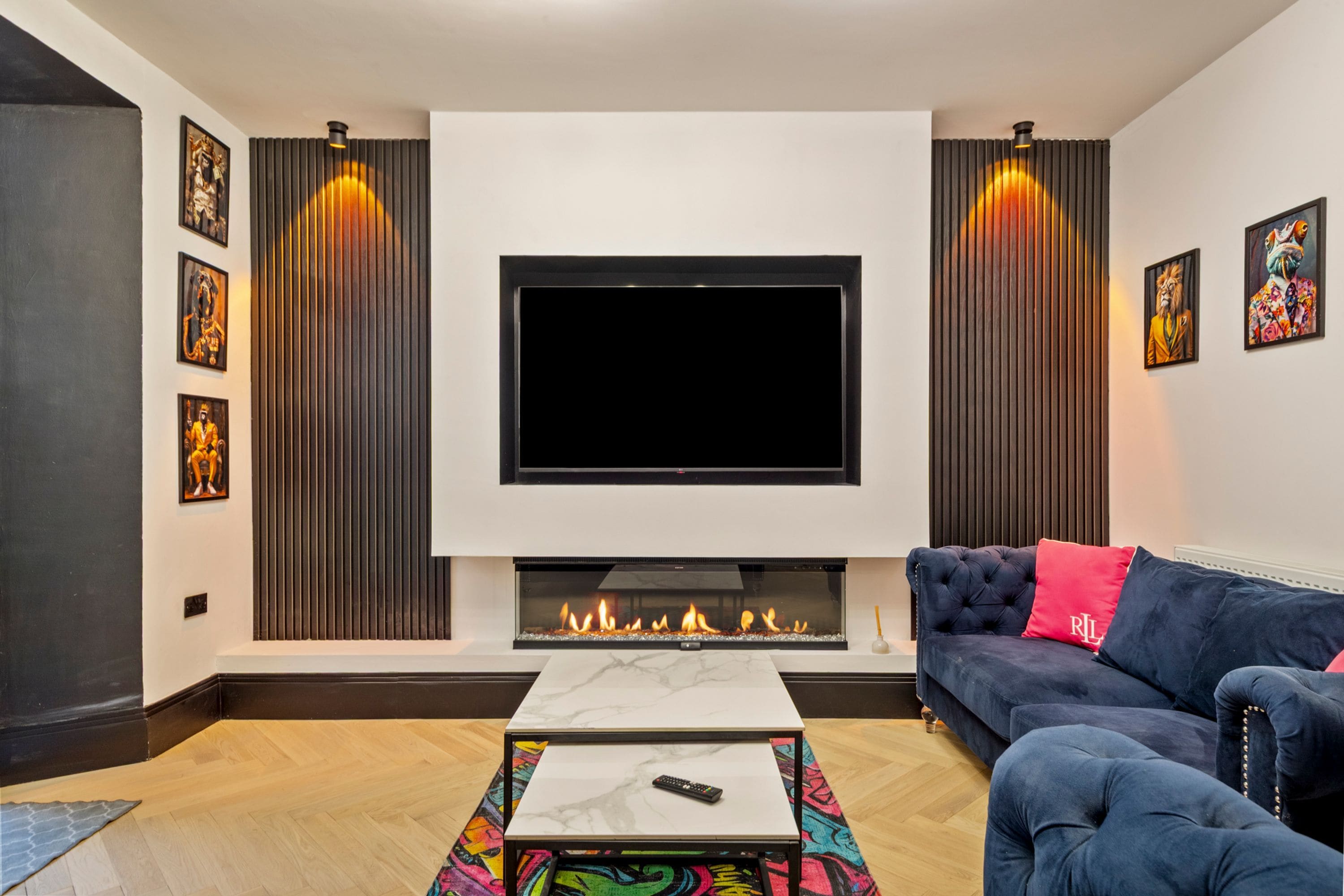 Een moderne woonkamer met een flatscreen televisie, een open haard, een bank en kunstwerken aan de wanden.
