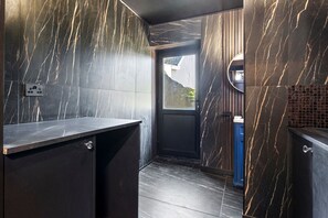 Une salle de bain moderne avec des murs en marbre foncé, un lavabo et une porte donnant accès à l’espace douche.