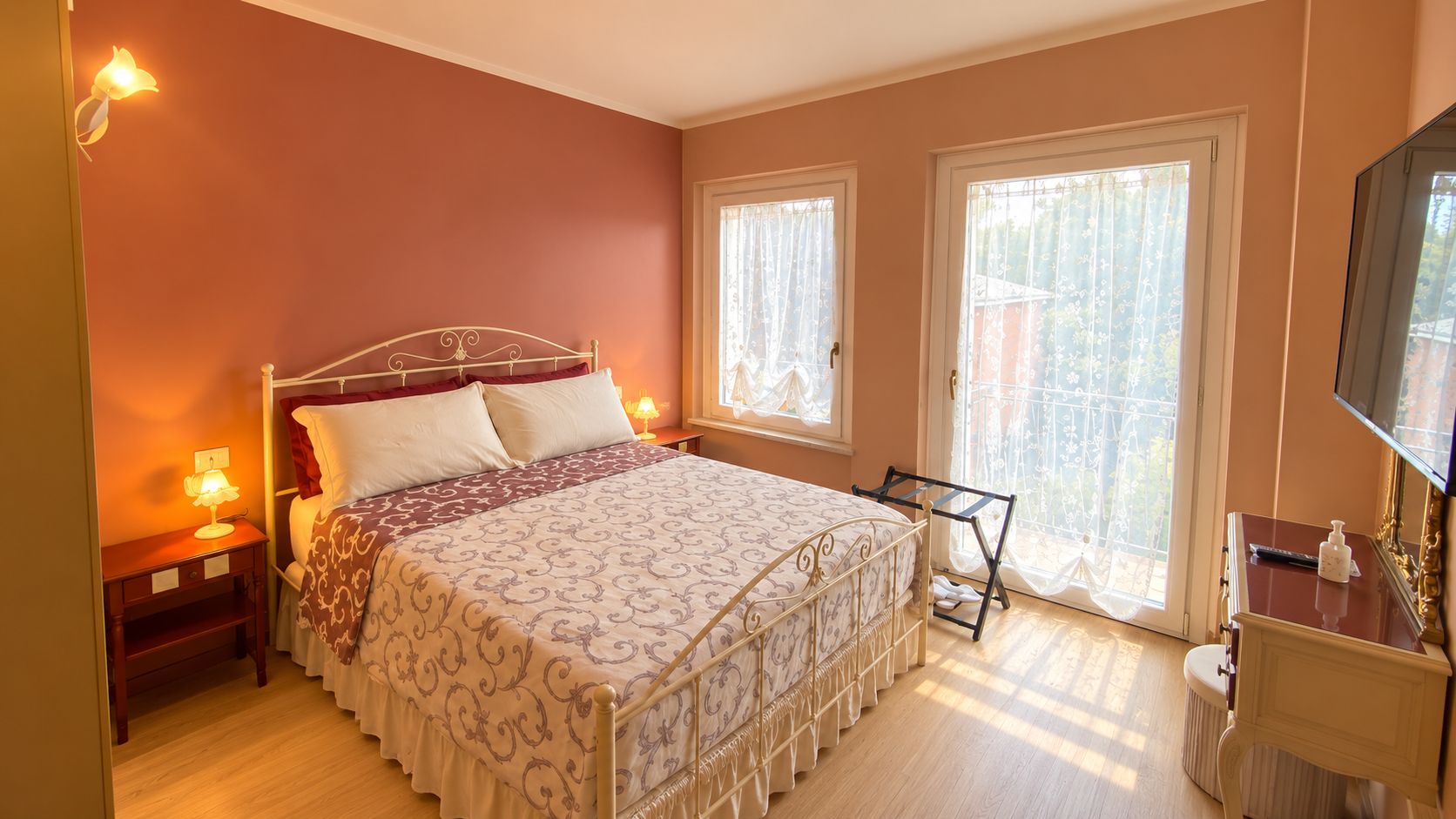 A bedroom with a four-poster bed, a bedside table with a lamp, a dresser, and a large window with curtains.