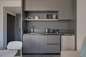 Eine kompakte Küche mit grauen Schränken, einer Mikrowelle, einer Kaffeemaschine und einem kleinen Kühlschrank.