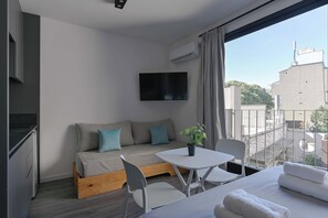 Ein modernes Zimmer mit einer Couch, einem kleinen Tisch, einem Fernseher und einem Balkon mit Blick auf Gebäude.