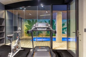 A gym with a stationary bike, a treadmill, and a wall mural of a tropical scene. - MOT Rentals + Design SohoHaus '305' - 3 pax Full Amenities (Buenos Aires)