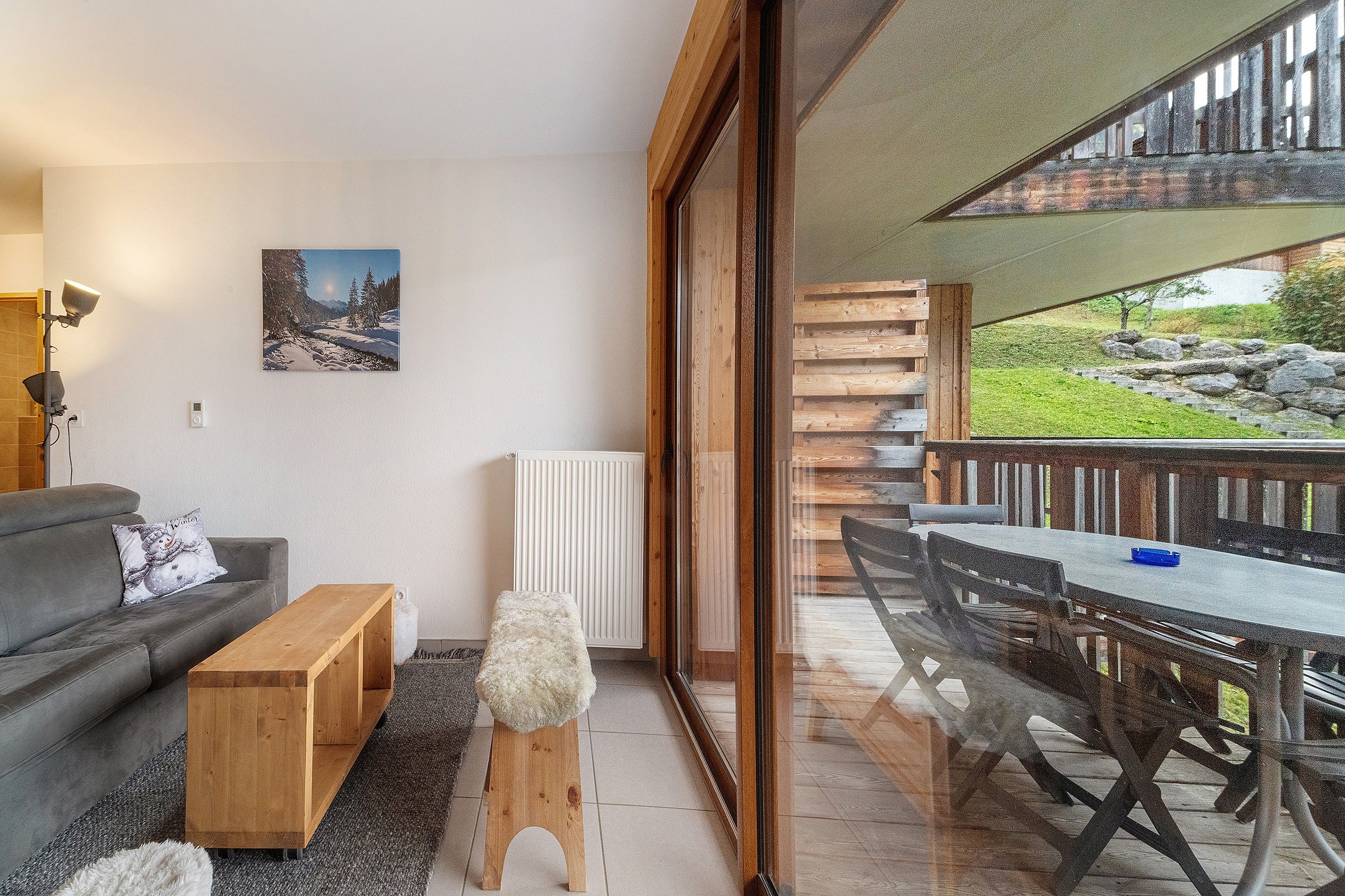 A modern living room with a sofa, coffee table, and a view of a balcony with outdoor furniture.