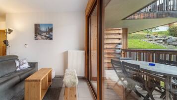 A modern living room with a sofa, coffee table, and a view of a balcony with outdoor furniture.