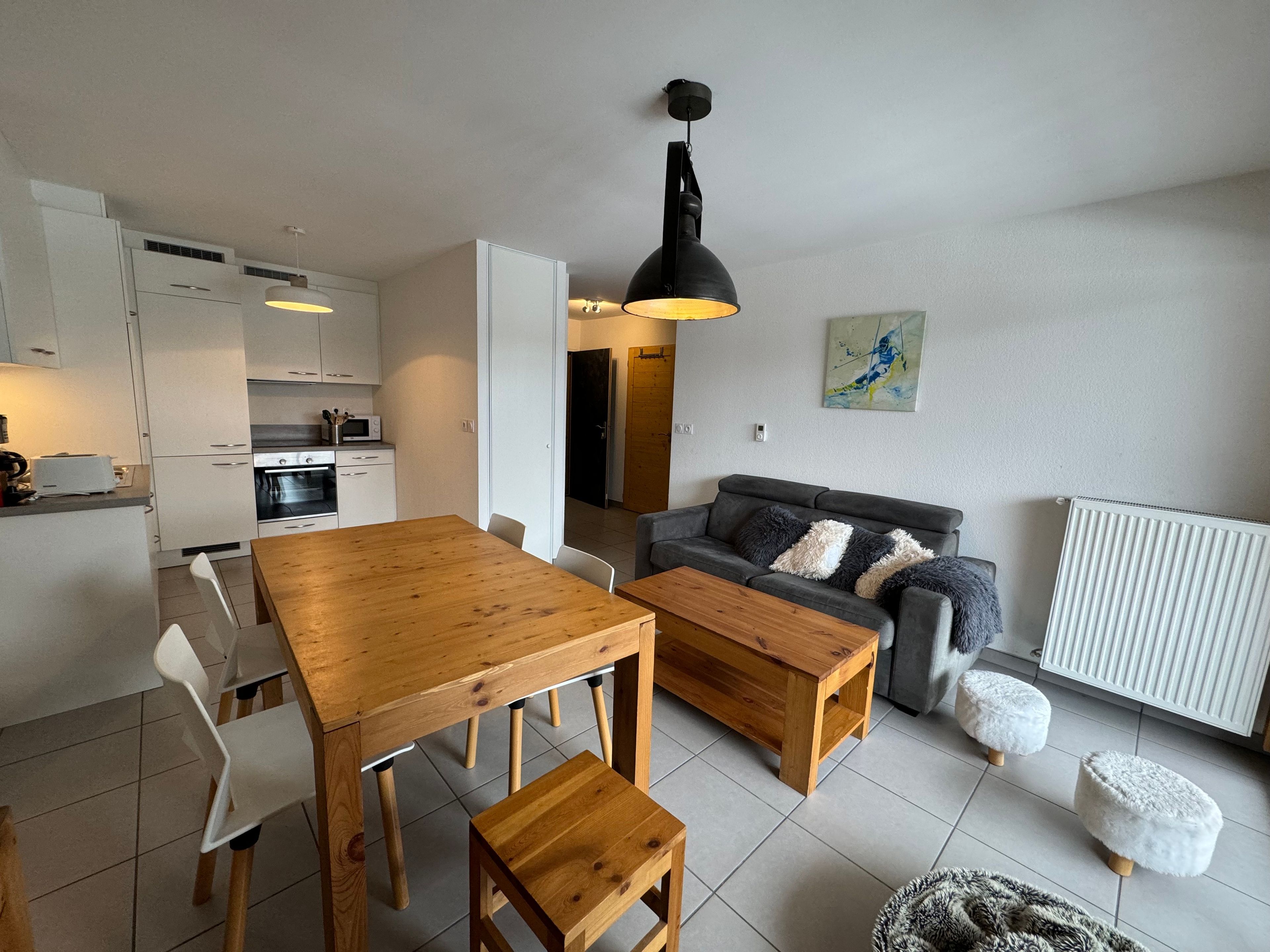 Un apartamento moderno con una mesa de comedor de madera, sillas blancas, un sofá gris con cojines mullidos y una lámpara colgante negra.