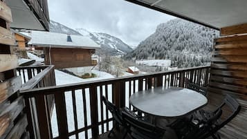 Una terraza de madera con una mesa y sillas, con vistas a un paisaje montañoso nevado.