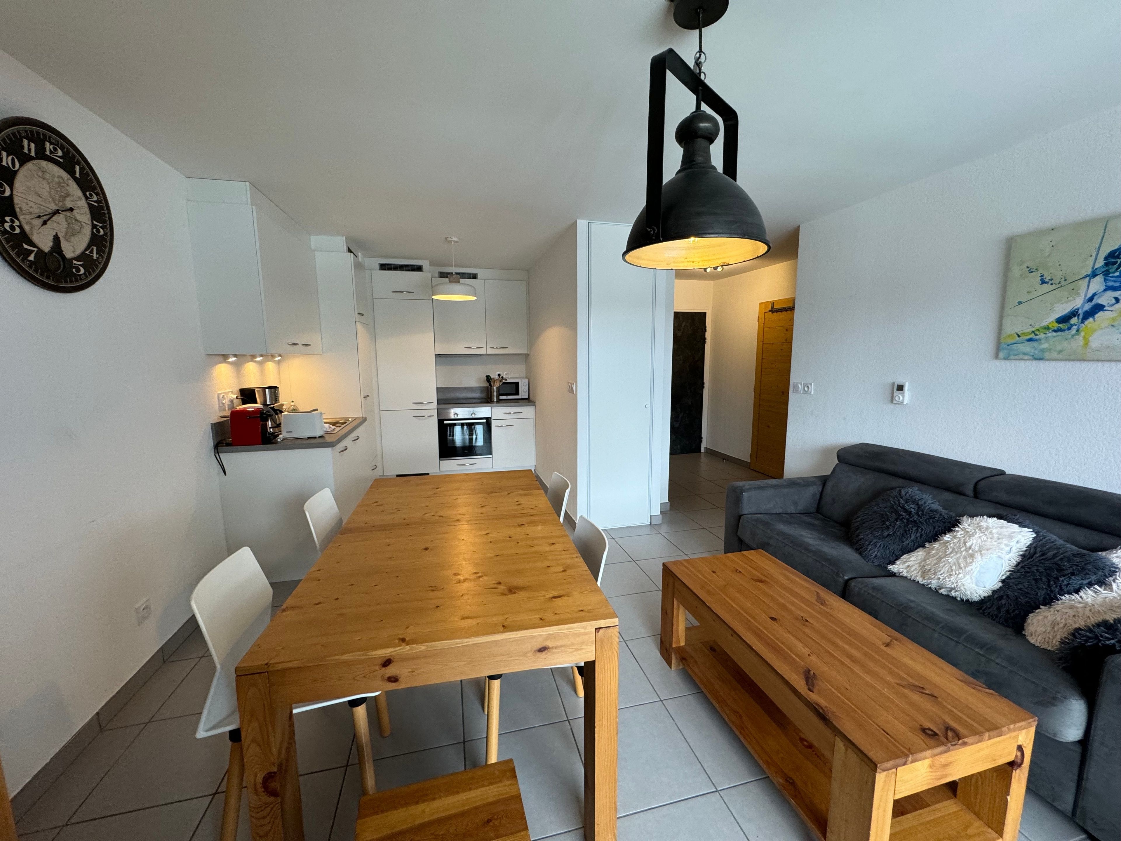 A modern living room with a wooden dining table, a sofa, and a black pendant light.