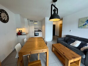 Een moderne woonkamer met een houten eettafel, een bank en een zwarte hanglamp.