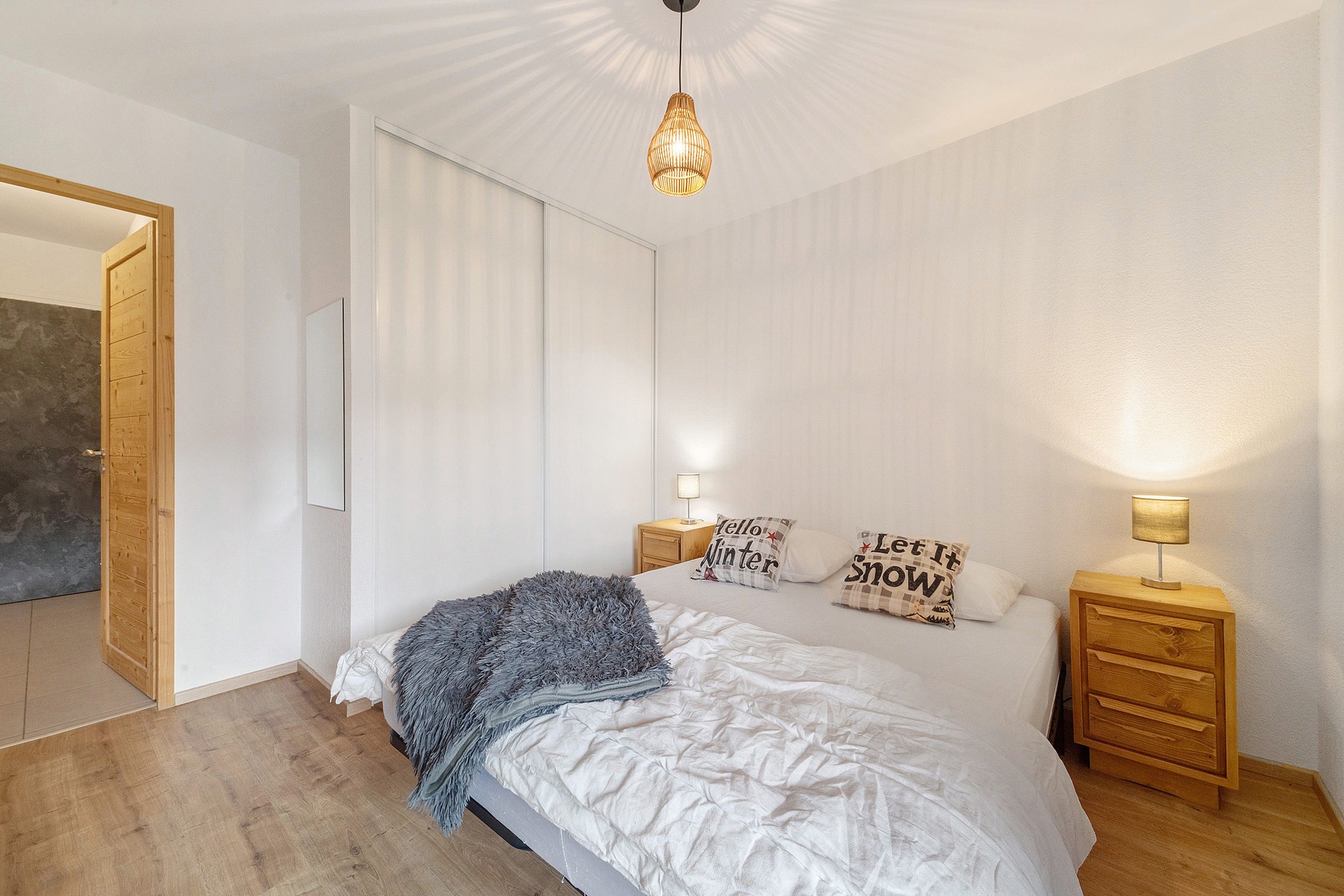 Ein Schlafzimmer mit einem Bett, zwei Nachttischen, einer Hängelampe und einer Tür.