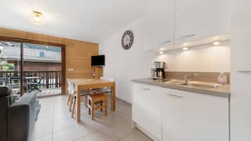 A modern kitchen with white cabinets, a wooden dining table, and a coffee maker.