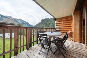Terraza de madera con mesa y sillas, con vista a un paisaje montañoso.
