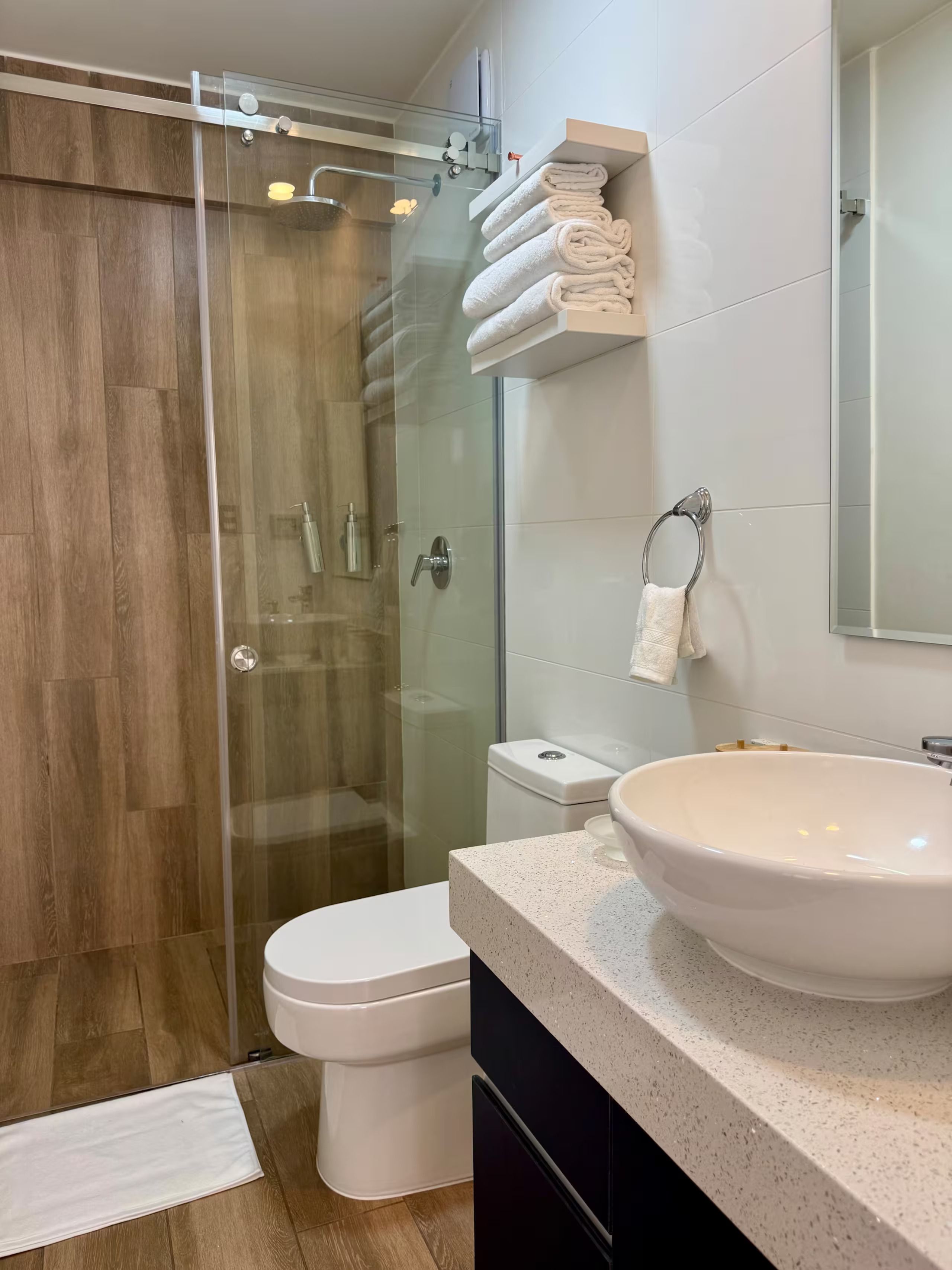 Une salle de bain moderne avec une douche à parois de verre, des toilettes blanches, un grand lavabo et un porte-serviettes.