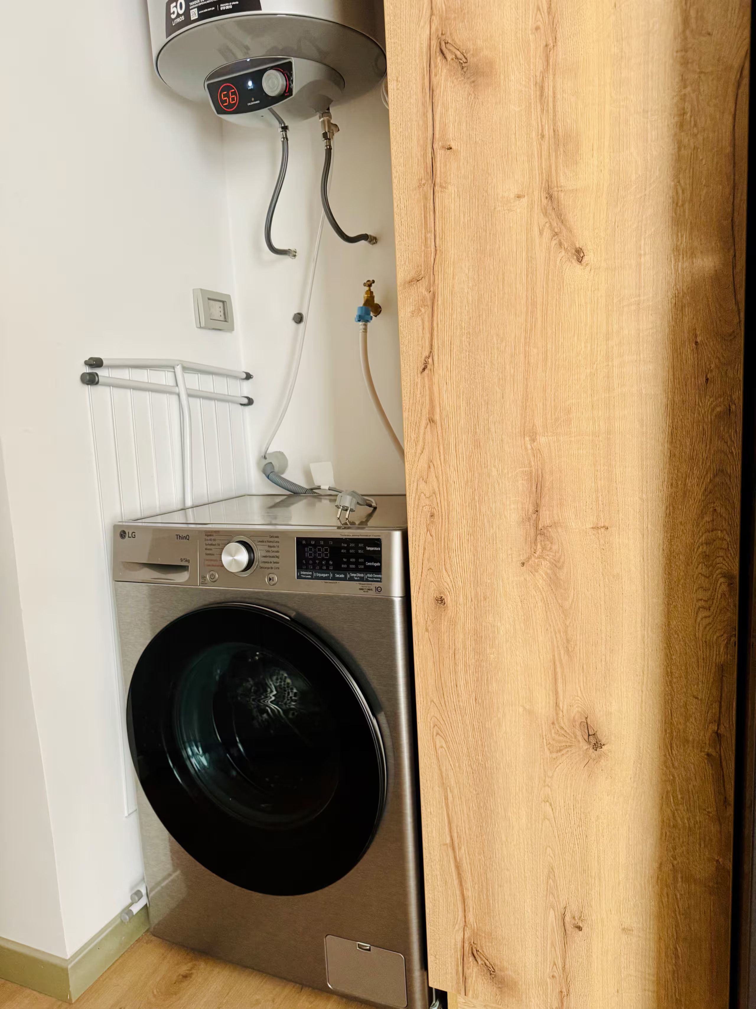 A compact, stainless steel LG ThinQ washing machine in a small laundry room with a white radiator and a wooden door.