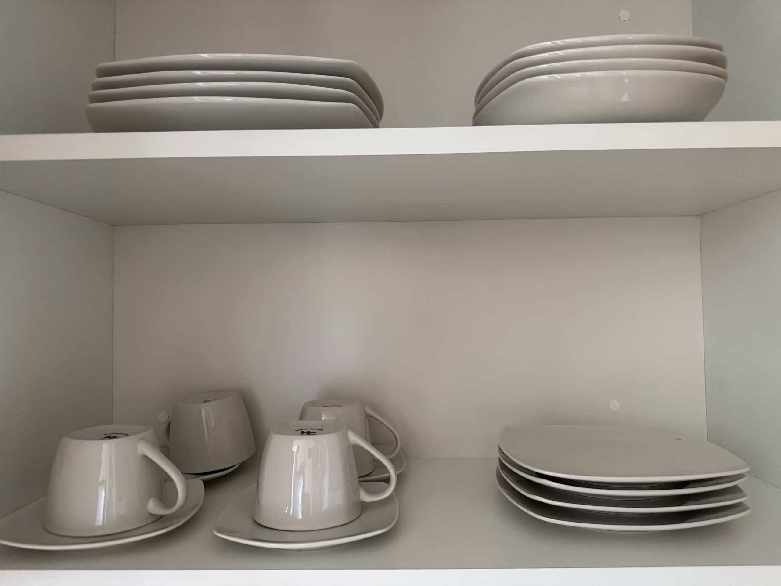 Une étagère blanche avec des assiettes et des tasses empilées.