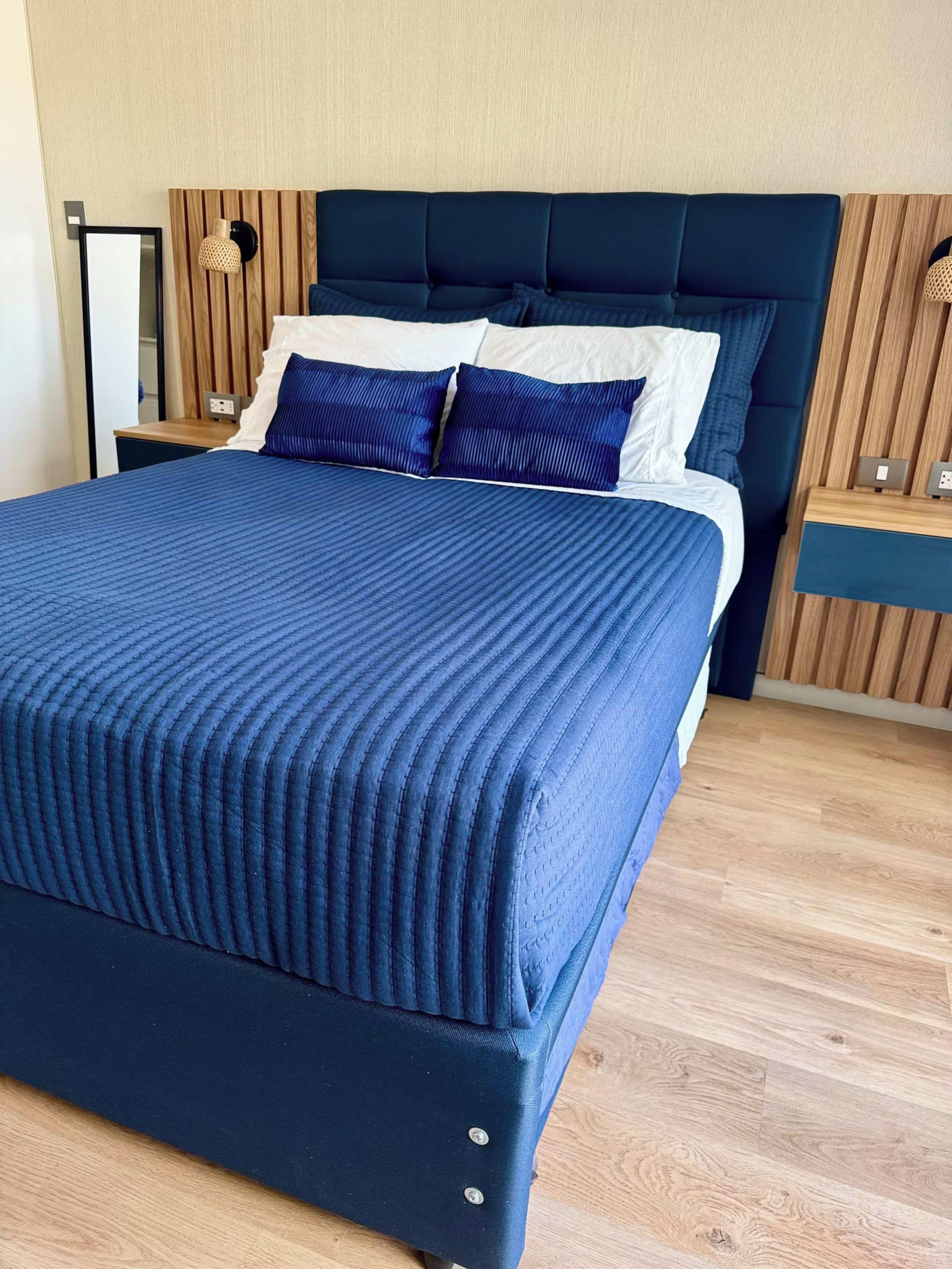 Una cama con cabecera tapizada en azul oscuro y colcha a juego.