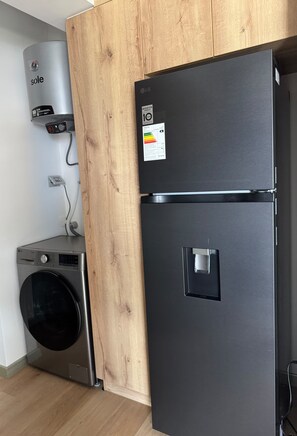 A compact kitchen with a stainless steel washing machine, a black refrigerator, and a water heater.