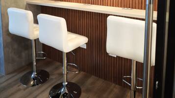 Un espace bar avec trois tabourets de bar blancs, un mur en lambris de bois et des luminaires suspendus.