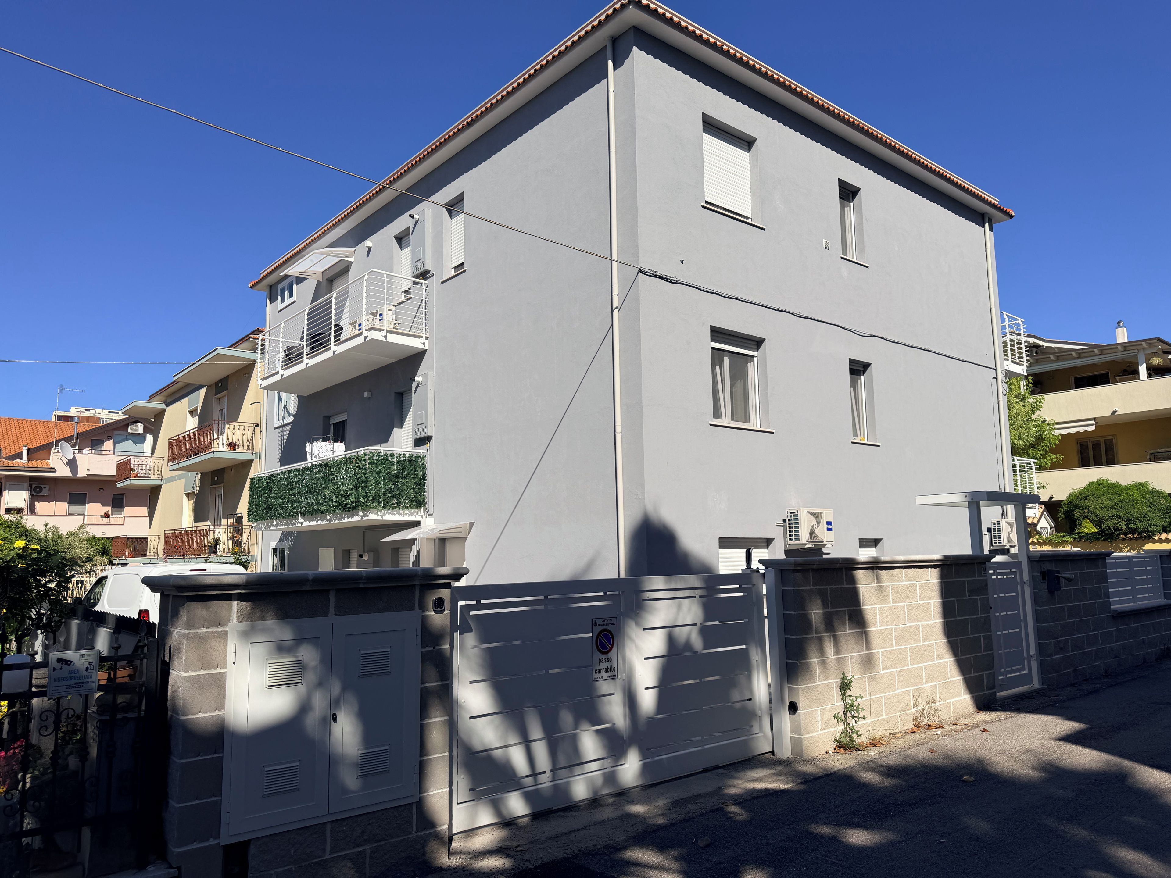 A two-story residential building with a balcony, a gated entrance, and a clear sky.