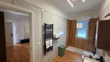 Une salle de bain moderne avec un plancher en bois, un mur en marbre, un porte-serviettes noir, une poubelle verte et un lavabo blanc.