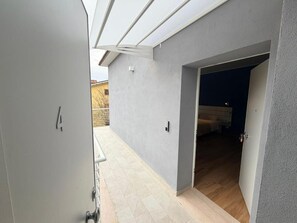 Un couloir avec une porte donnant sur une pièce où se trouvent un lit et une fenêtre.