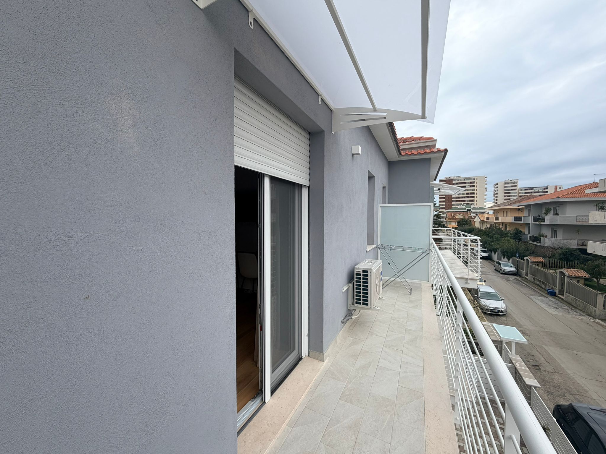 A balcony with a view of a residential street, a closed sliding door, and a small air conditioning unit.