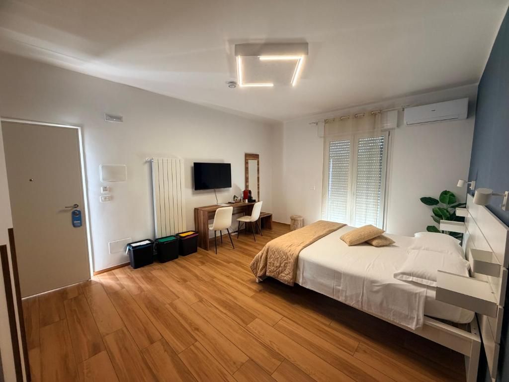 Une chambre à coucher comprenant un lit, un bureau, une chaise, un téléviseur et une fenêtre avec des stores.