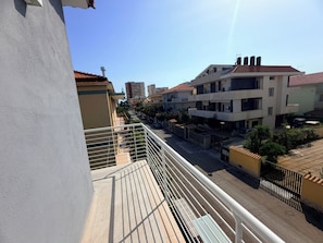 Una calle residencial con edificios, cielo despejado y un balcón con barandilla.