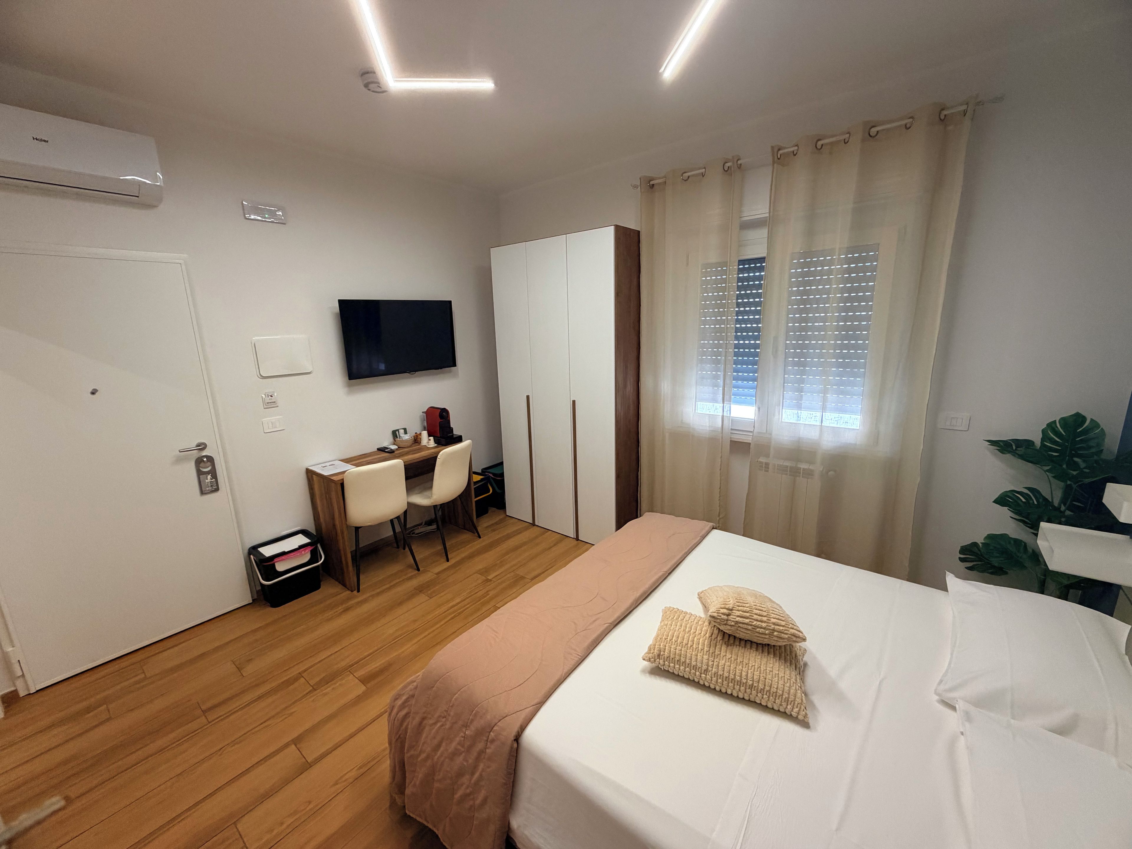 Ein Hotelzimmer mit einem Bett, einem Schreibtisch mit Stühlen, einem Fernseher und einem Fenster mit Vorhängen.
