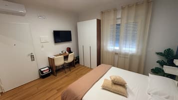 Una camera d'albergo con un letto, una scrivania con sedie, una televisione e una finestra con tende.