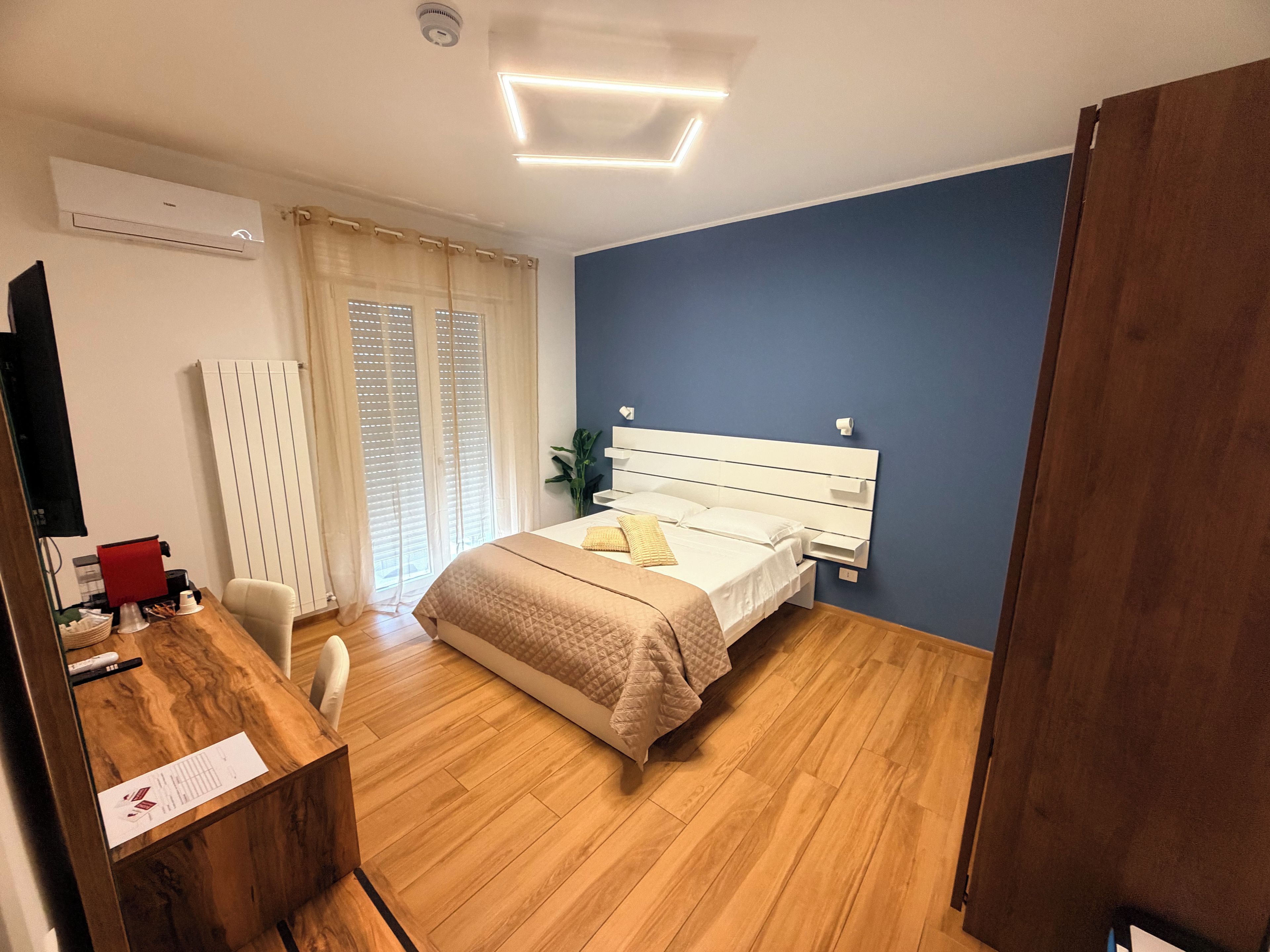 A bedroom with a bed, a desk, a chair, a radiator, and a window with curtains.