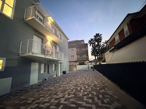 Un estrecho callejón con pavimento de ladrillo estampado, un edificio con balcón a la izquierda y una palmera al fondo.