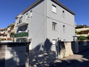 A two-story building with a gated entrance, a balcony with a railing, and a small garden area. - Palazzo del toro 2 (Montesilvano)