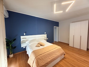 Une chambre à coucher comprenant un lit, une armoire, une plante en pot et un luminaire fixé au plafond.