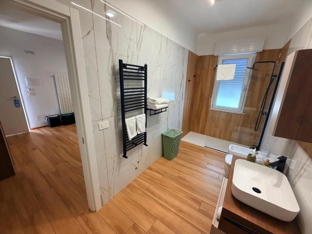 Un bagno moderno con pavimento in legno, un lavandino bianco, un porta asciugamani e una finestra.