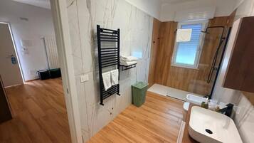 Un bagno moderno con pavimento in legno, un lavandino bianco, un porta asciugamani e una finestra.