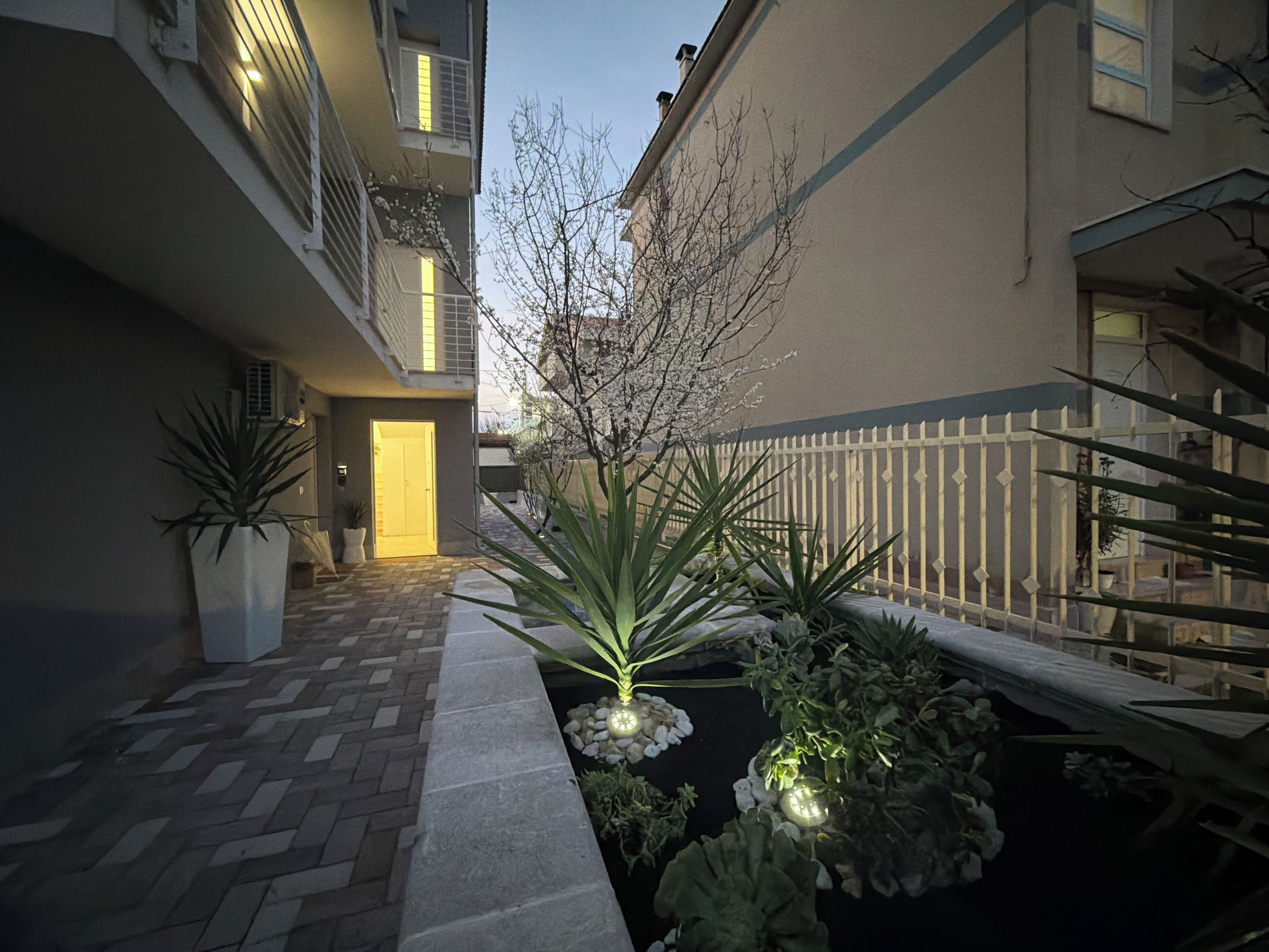 A courtyard with a paved walkway, a white fence, and potted plants.