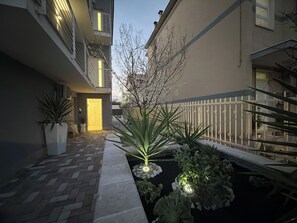 Un patio con sendero empedrado, cerca blanca y plantas en macetas.