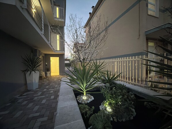 Une cour avec un chemin pavé, une clôture blanche et des plantes en pot.