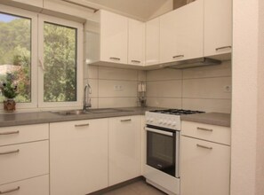 A kitchen with white cabinets, a gas stove, and a window with a view of greenery. - Paradise Apartments-studio Apartment With sea View and Balcony 5 (Jelsa)