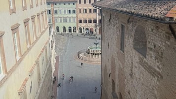 Una piazza storica con edifici in pietra, una fontana e cielo sereno.