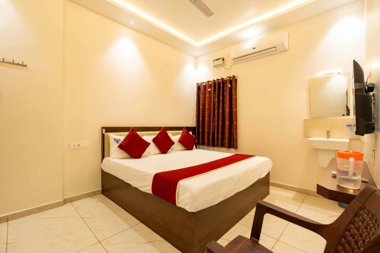 Habitación de hotel con cama, escritorio, silla, aire acondicionado, televisor y baño con lavamanos y espejo.