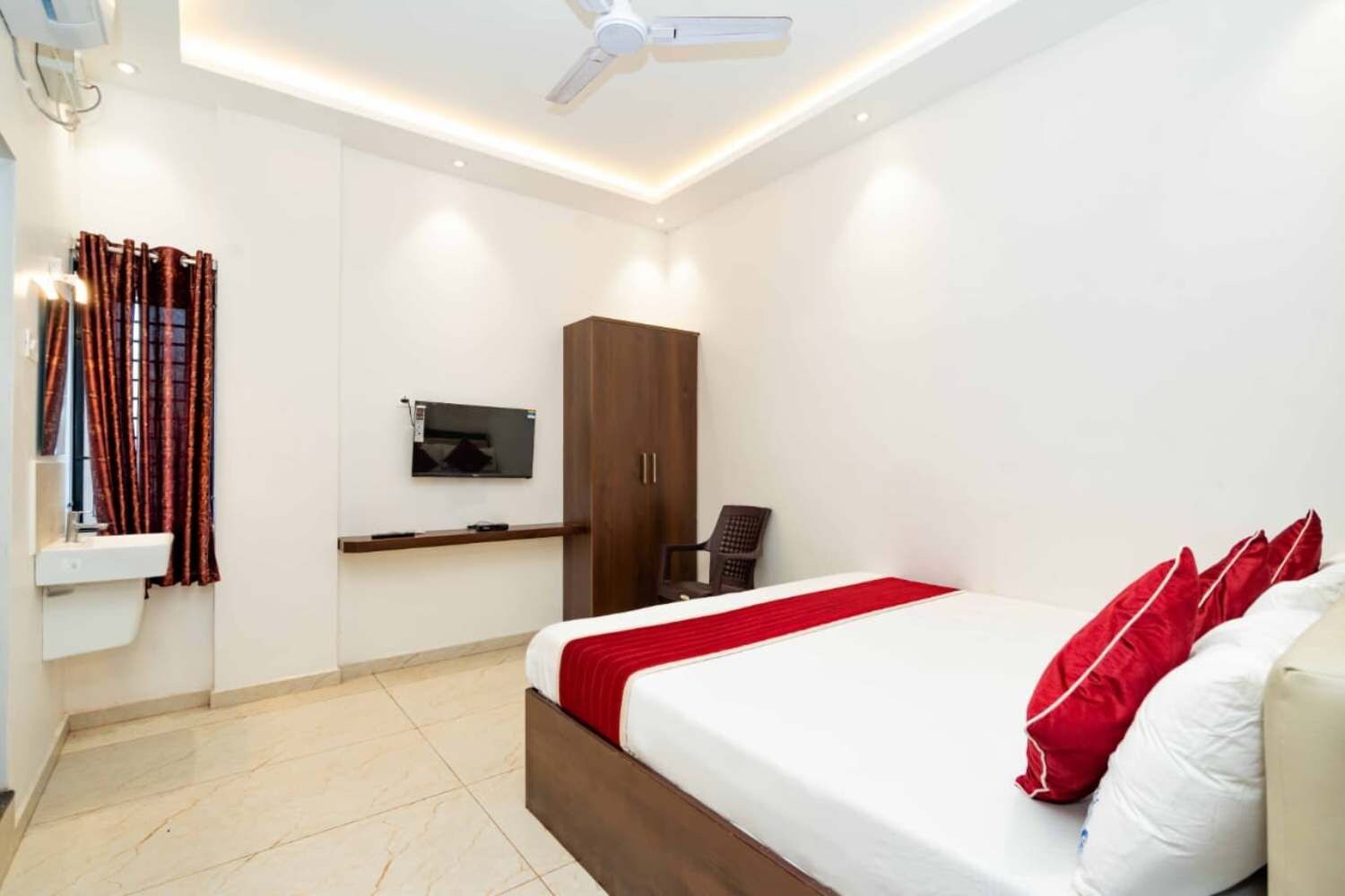 Una habitación de hotel con cama, televisión montada en la pared, armario y ventilador de techo.