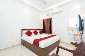 A hotel room with a bed, a television, a desk with a lamp, and a bathroom with a mirror. - VNY Grand (Rameshwaram)