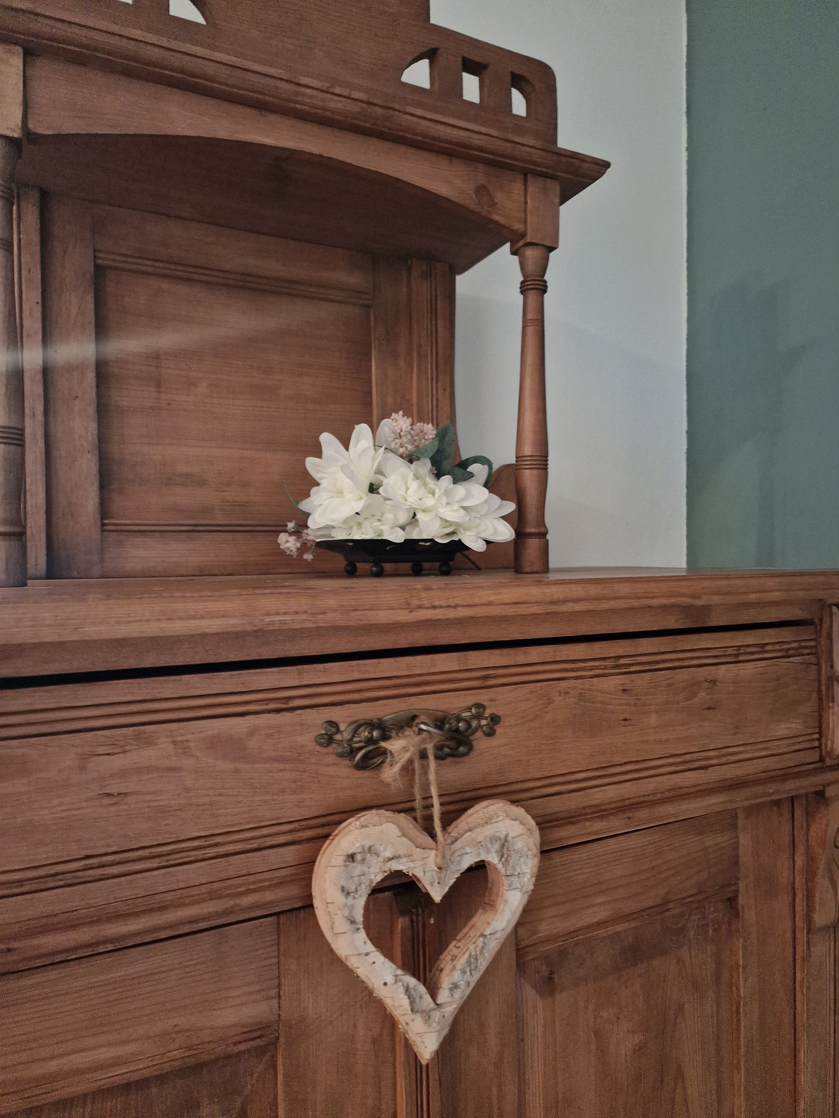 En byrå i trä med en hjärtformad dekoration och en vas med blommor ovanpå.