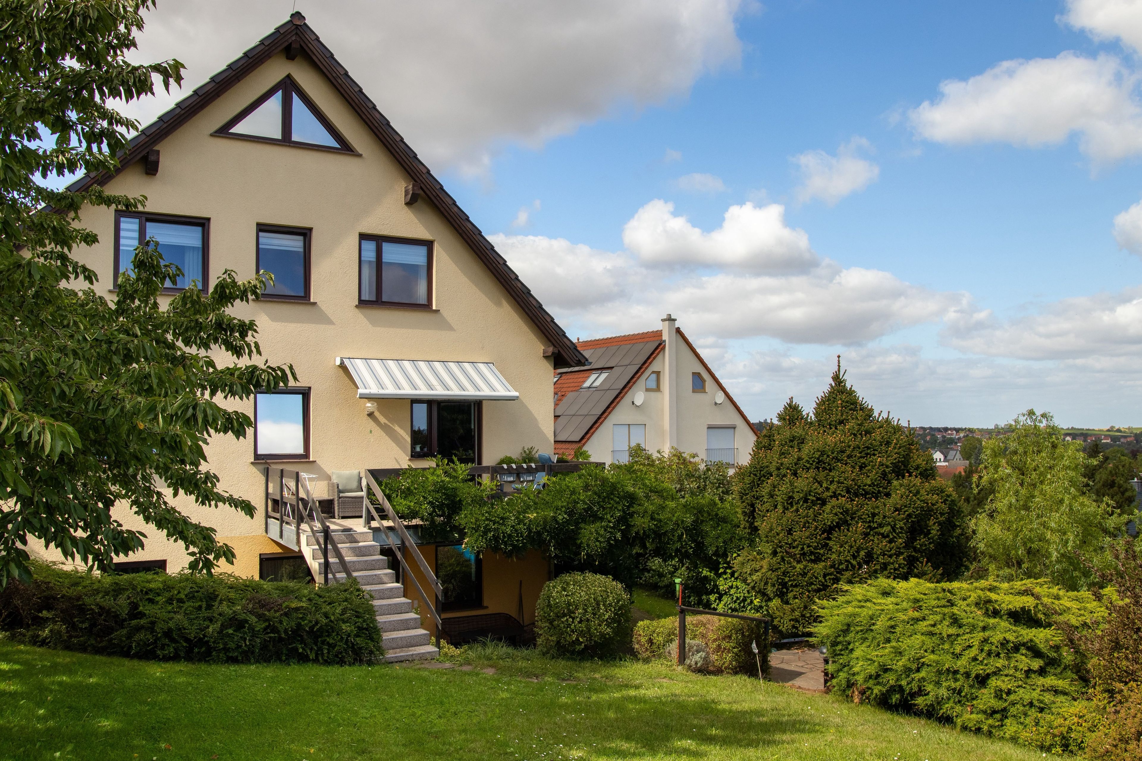 Een tweelaags huis met een schuin dak, een zichtbare trap en een verzorgde tuin.