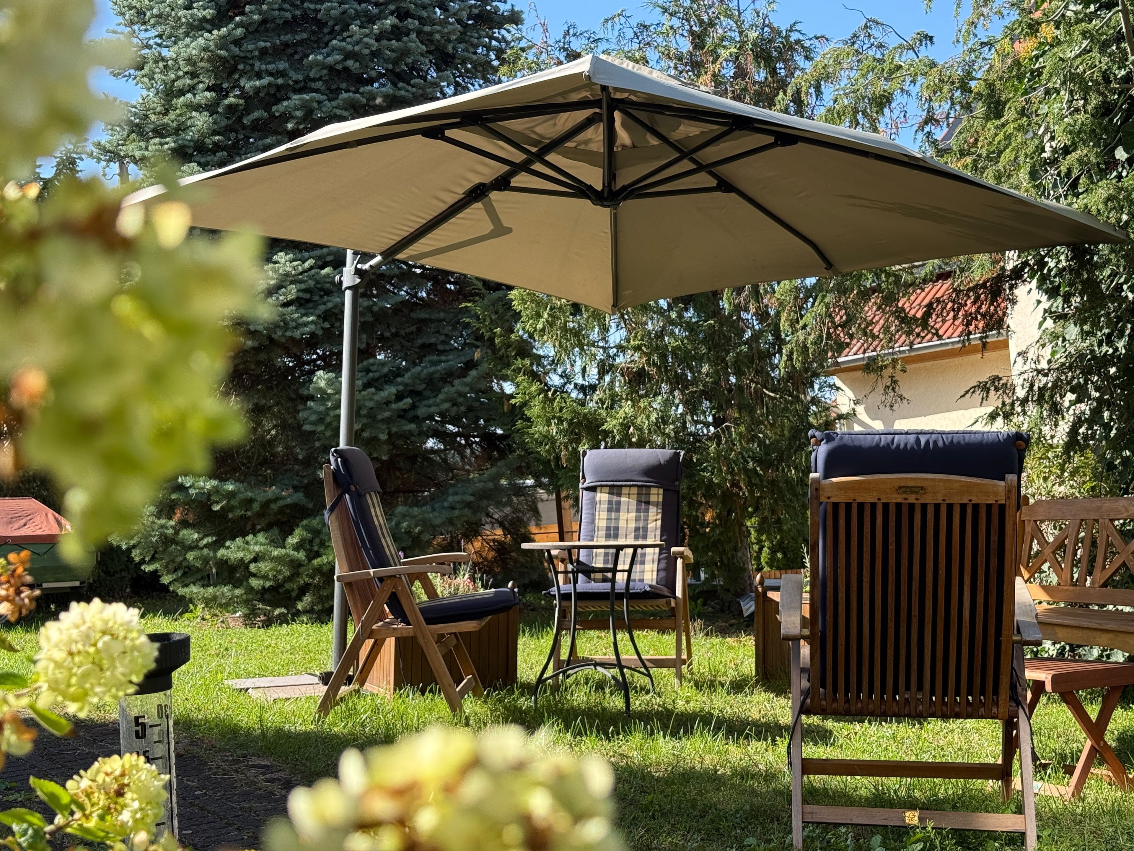 Ein Sitzbereich im Freien mit einem großen Sonnenschirm, Holzstühlen und einem Tisch.