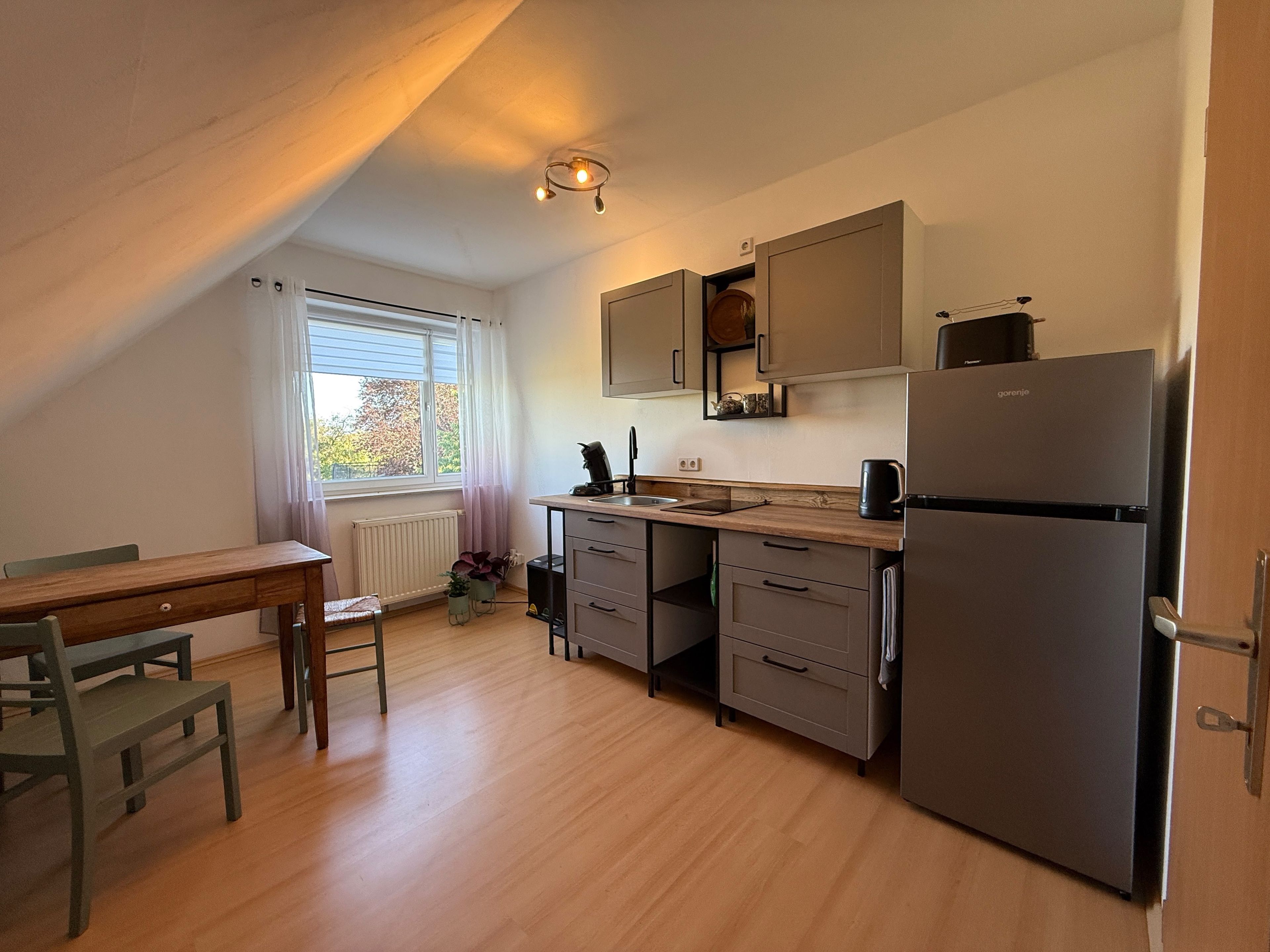 Una cucina compatta con un tavolo di legno, sedie, un frigorifero e mobili.