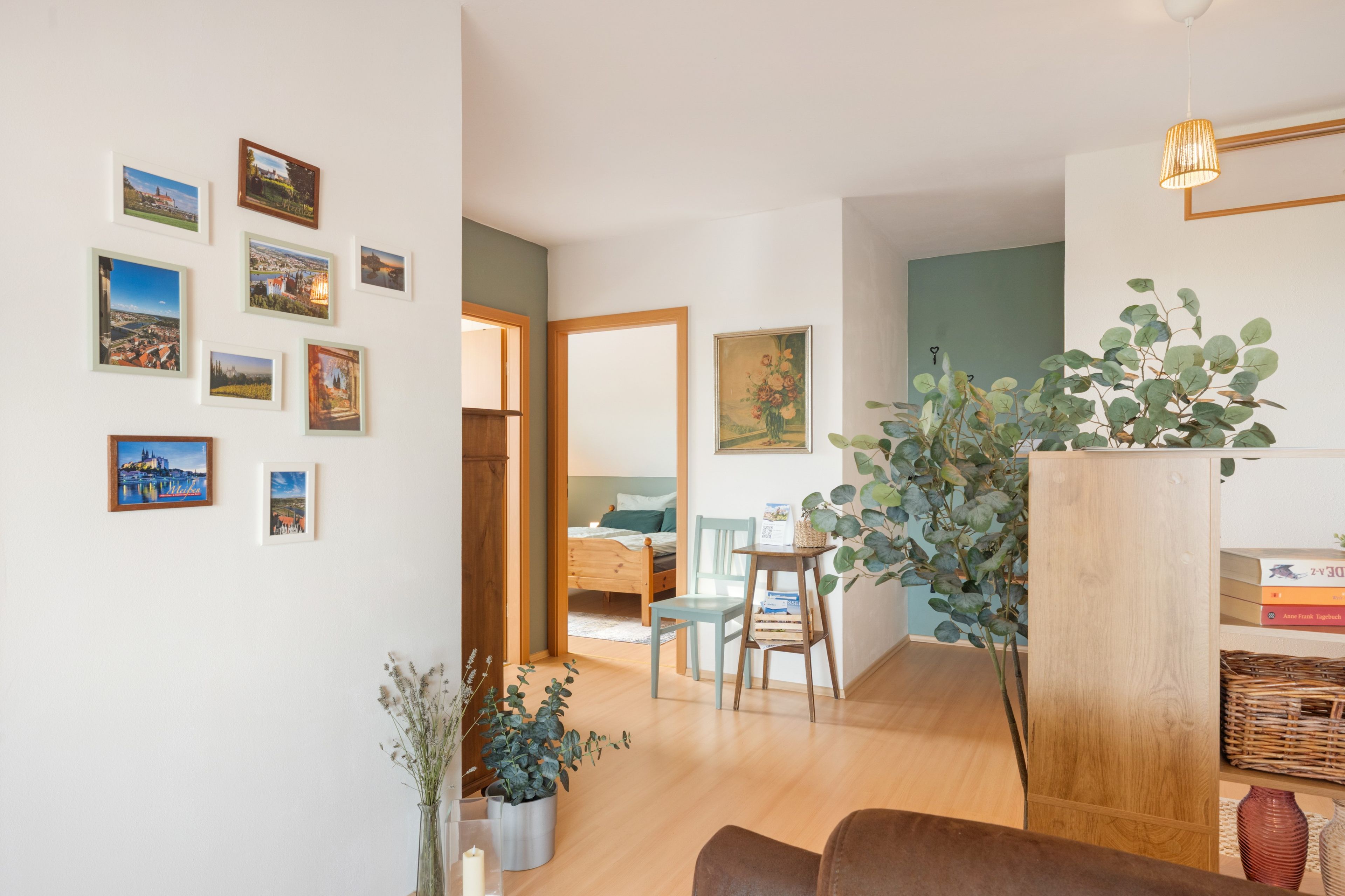 A room with a bed, a wooden floor, a chair, a table, and a potted plant.