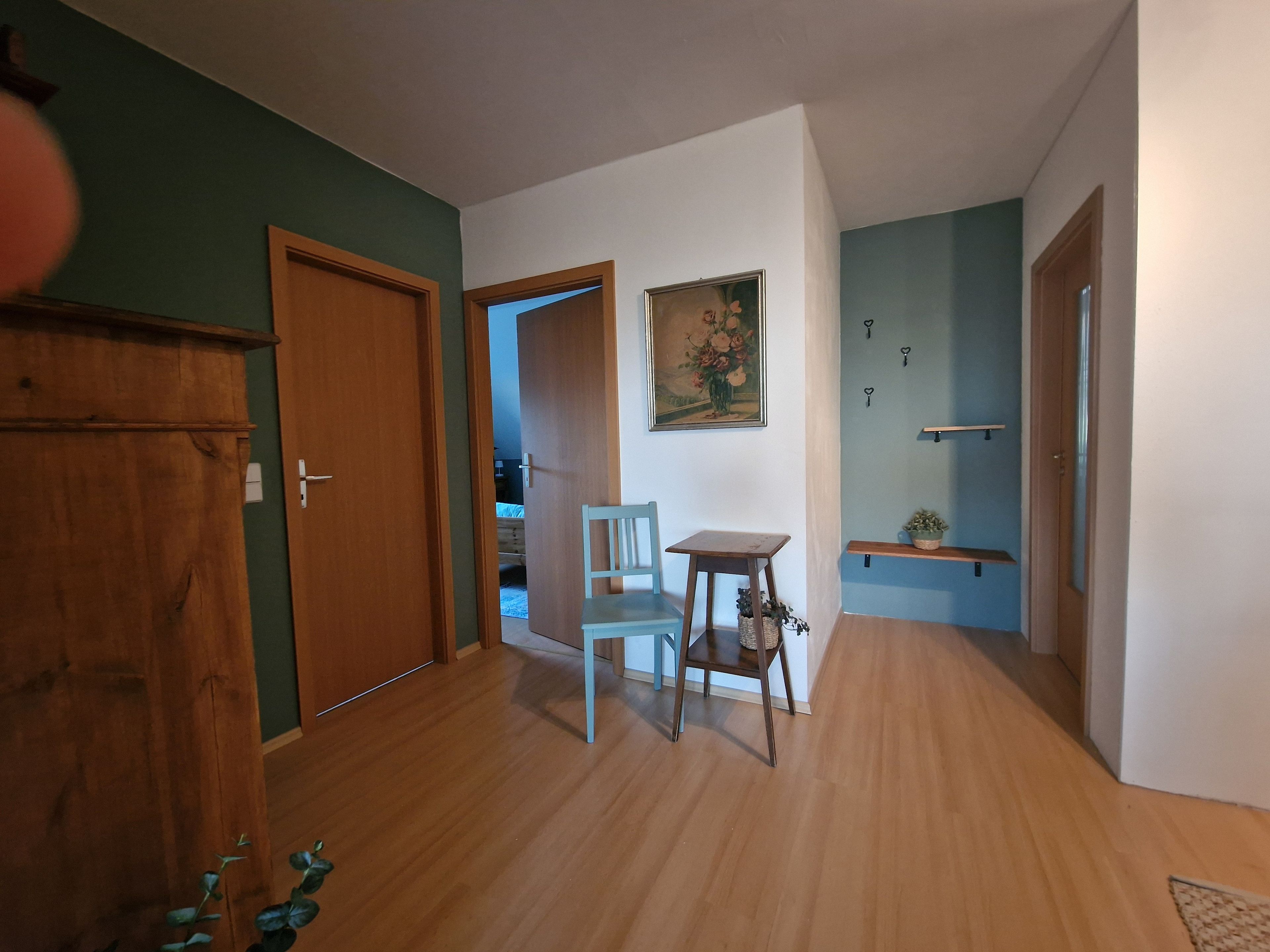 Ein Flur mit Holzboden, einem Holzschrank, einem Sessel, einem kleinen Tisch und einem Bild an der Wand.
