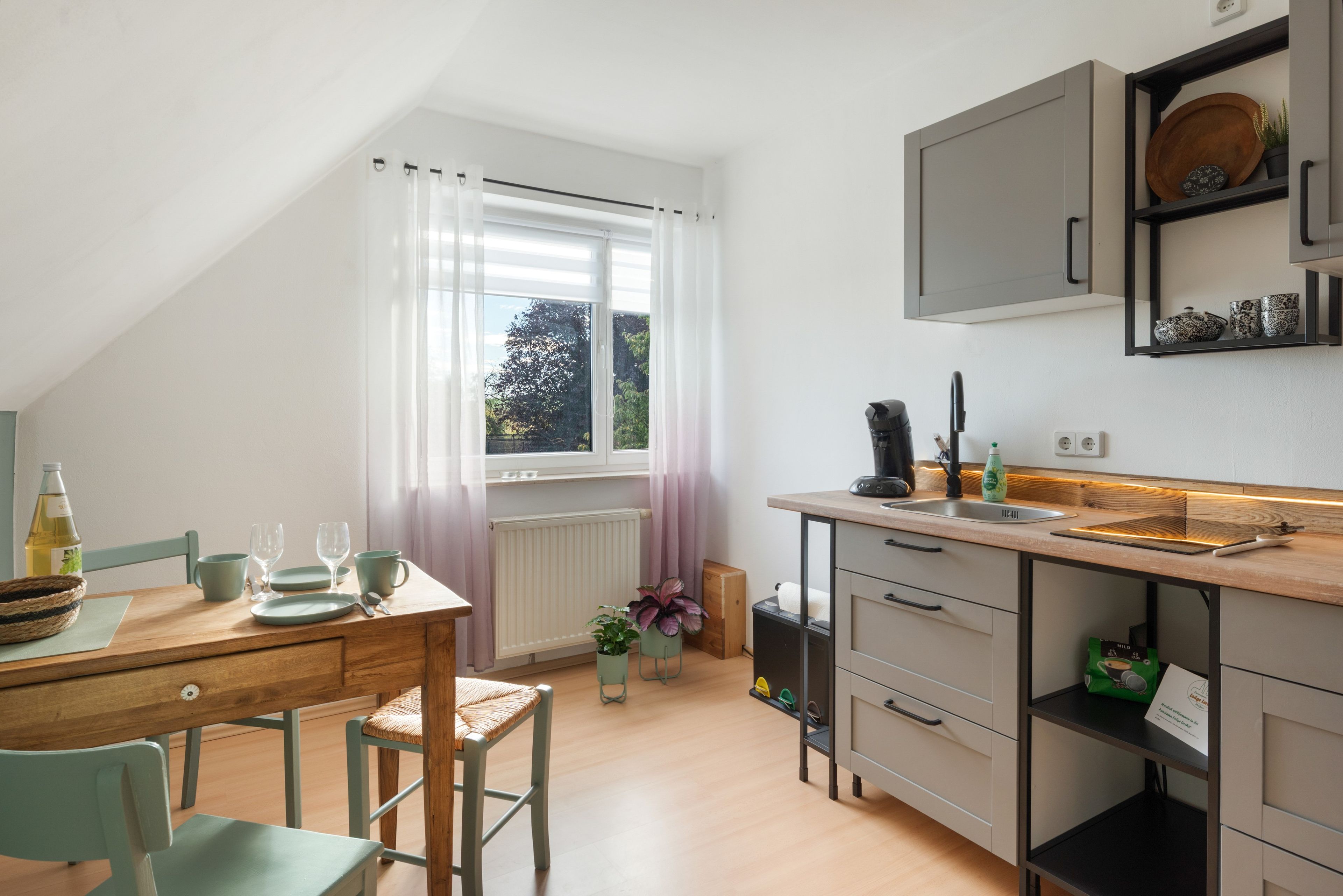 Eine moderne Küche mit Essbereich, ausgestattet mit einem Holztisch, Stühlen und einem Fenster mit Vorhängen.